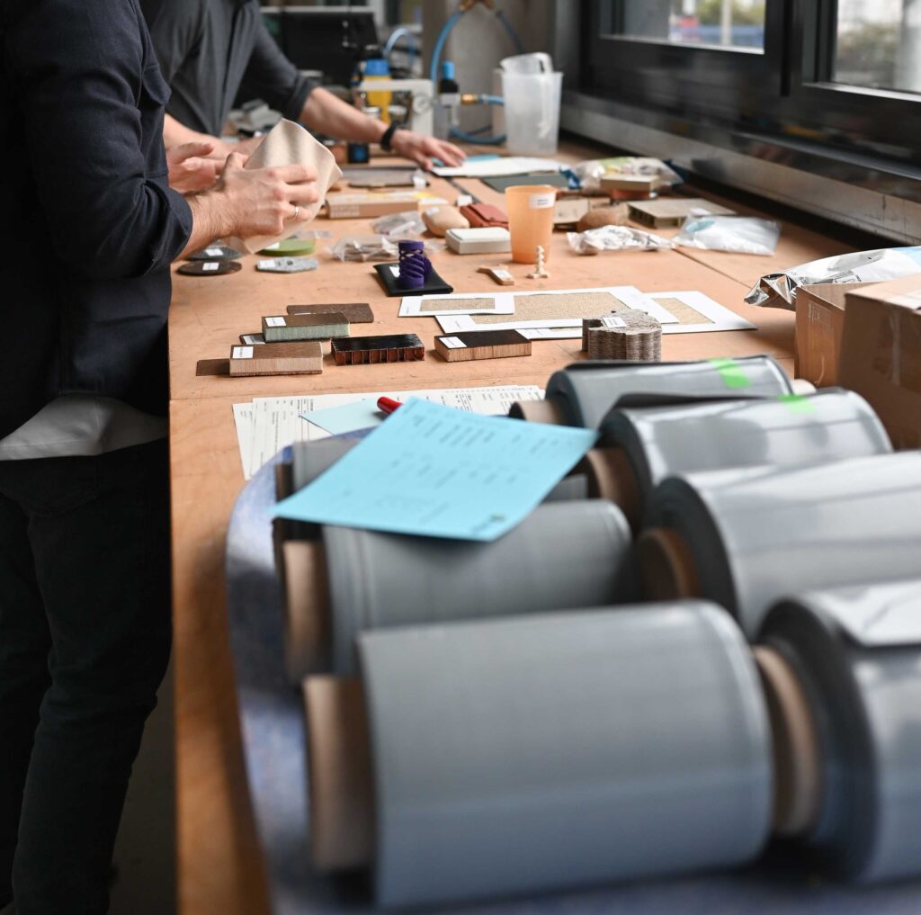 Einblick in einen Teil der Materialsammlung von Offsee: Person betrachtet auf einer Werkbank ausgelegte Materialproben.