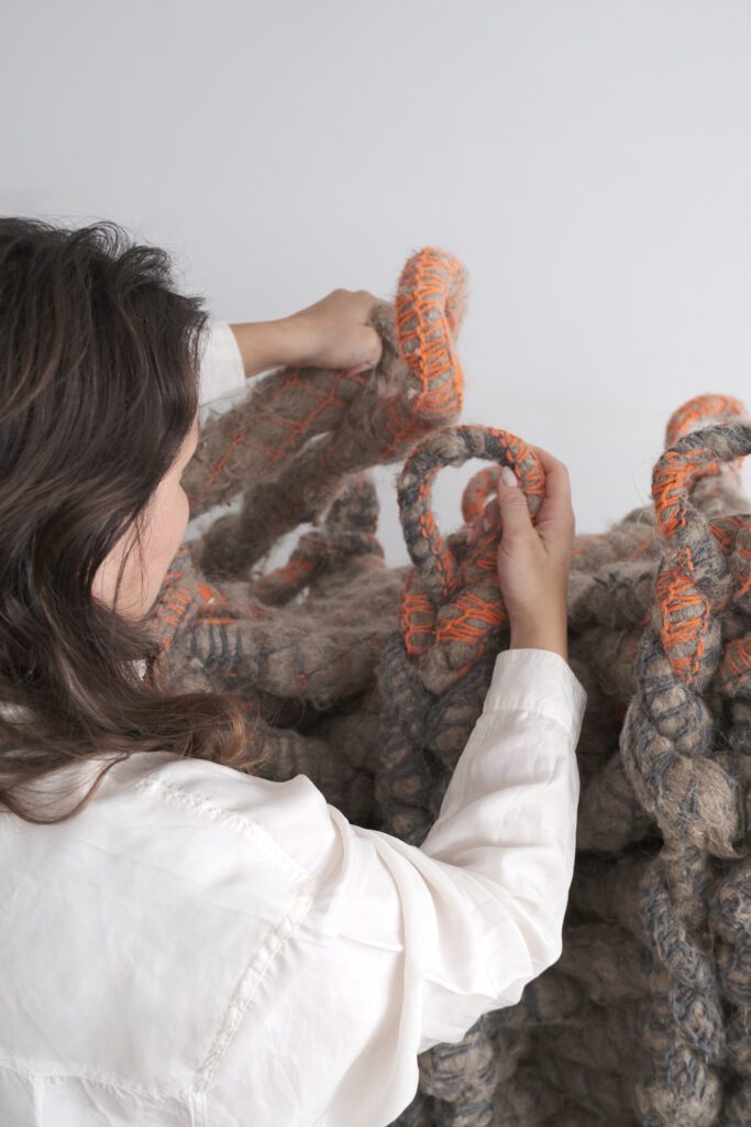 A person is working on an installation made of thick, fabric-like tubular elements, weaving them together into a net-like mesh.