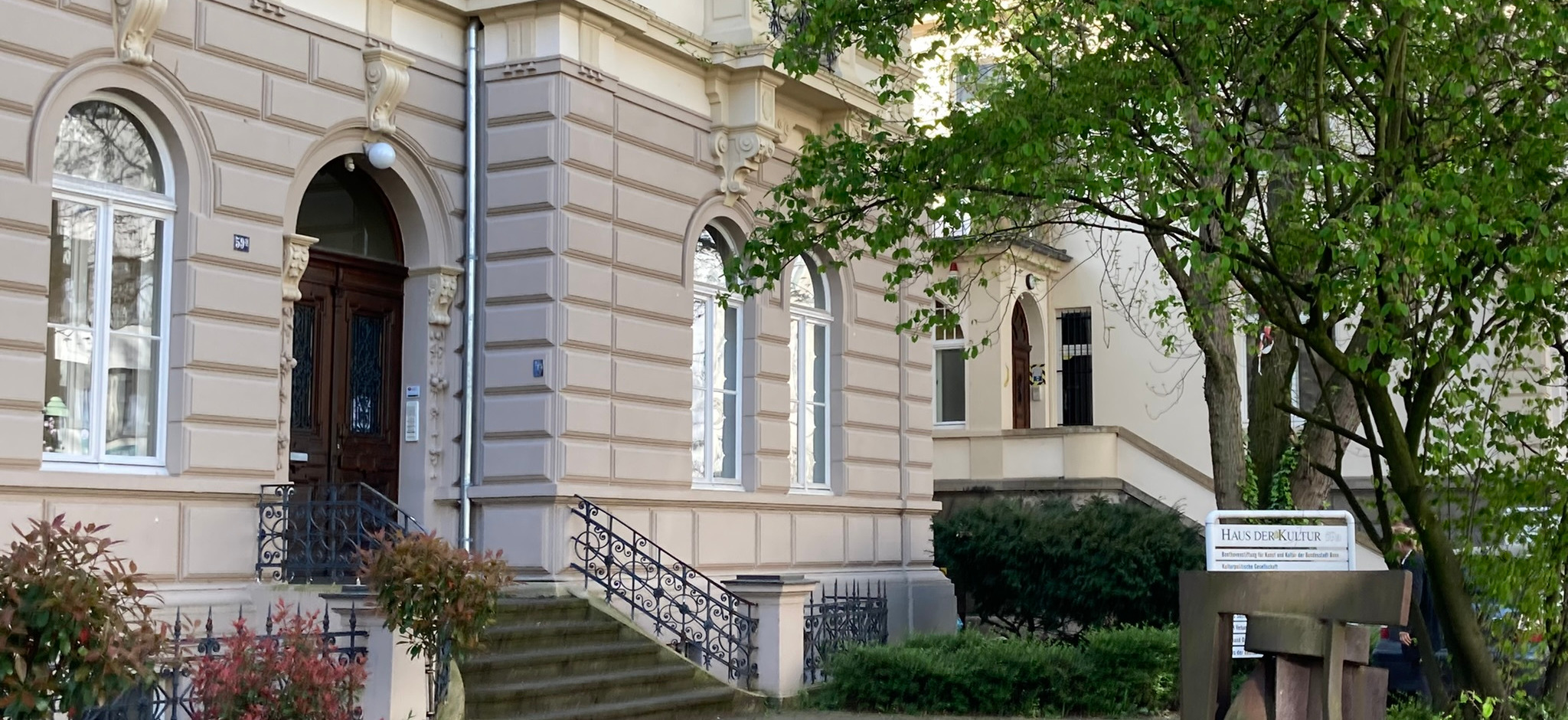 Außenansicht des Hauses der Kultur in Bonn mit historischer Fassade, Eingangstreppe und einem Schild im Vordergrund mit der Aufschrift “HAUS DER KULTUR / Kulturpolitische Gesellschaft e.V.”.