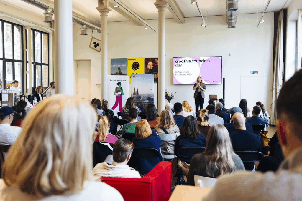 Kreativschaffende beim creative founders day von creative.nrw im Filmhaus Köln: Zahlreiche Teilnehmende sitzen in einem hellen Veranstaltungsraum und verfolgen eine Präsentation auf einer Leinwand.