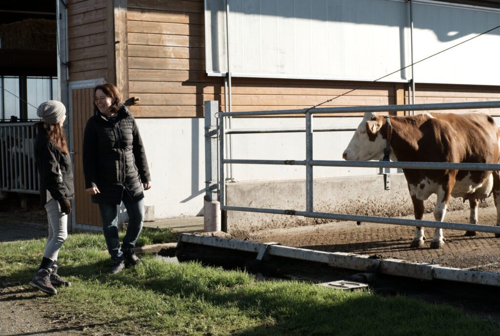 Two women are standing in front of a cow's pen at a family-run dairy farm. The photo offers a glimpse into the day-to-day work of a farm.