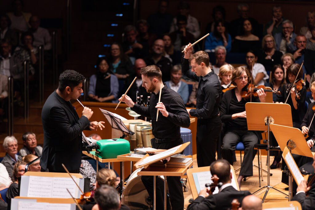 Musiker des Orchesters und Schlagzeuger spielen auf klassischen Instrumenten sowie auf Alltagsgegenständen und wiederverwendeten Materialien. Das Konzert verbindet zeitgenössische Musik mit dem Thema Nachhaltigkeit.